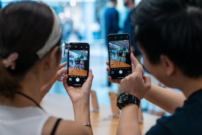 © Bloomberg. An employee, right, demonstrates the camera function on the Apple Inc. iPhone XS Max, right, and the iPhone XS at an Apple store during its launch in Hong Kong, China, on Friday, Sept. 21, 2018. The iPhone XS is up to $200 more expensive than last year's already pricey iPhone X and represents one of the smallest advances in the product line's history. But that means little to the Apple faithful or those seeking to upgrade their older iPhone. Photographer: Anthony Kwan/Bloomberg