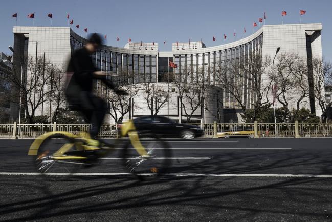 © Bloomberg. A man rides a bicycle past the People's Bank of China (PBOC) headquarters in Beijing, China, on Thursday, March 9, 2017. China's central bank plans to apply a stricter method for assessing banks' capital as part of efforts to contain financial-sector risks, people with knowledge of the matter said. Photographer: Qilai Shen/Bloomberg