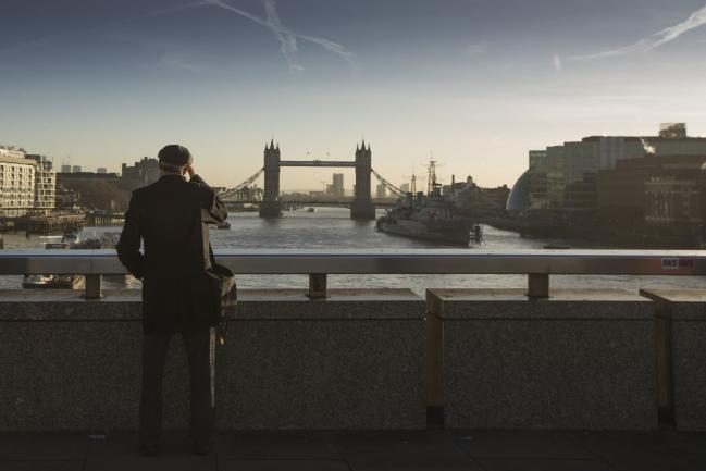 © Bloomberg. A commuter stops on London Bridge to view Tower Bridge in the distance in London, U.K., on Monday, Dec. 18, 2017. U.K. firms wanting workers face the tightest labor market in two decades. In 2011, there were almost six unemployed people for every vacancy; now there are fewer than two, the lowest ratio since records began in 2001. 