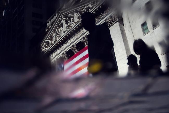 © Bloomberg. The silhouettes of pedestrians are seen in a puddle in front of the New York Stock Exchange