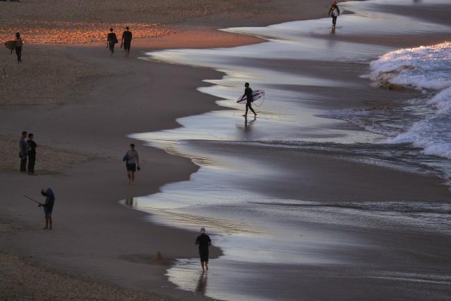 © Bloomberg. Beach goers and surfers gather on Bondi Beach at sunset in Sydney, Australia, on Wednesday, May 15, 2019. Australia's economy has been weighed down by a retrenchment in household spending as property prices slump and slash personal wealth. An election Saturday is likely to see the opposition Labor party win power and lift spending further. 