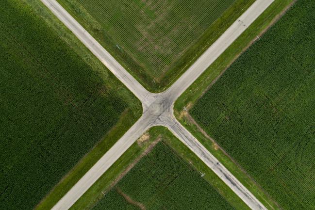 © Bloomberg. Soybean, top, and corn plants grow in fields bordering a rural intersection in this aerial photograph taken above Ohio, Illinois, U.S., on Tuesday, June 19, 2018. A rout in commodities deepened as the threat of a trade war between the world's two biggest economies intensified, hitting markets from steel to soybeans. Soybean futures were among the biggest losers, falling as much as 7.2 percent to the lowest in more than two years. Corn slipped to the lowest since January, while wheat and cotton also dropped. 