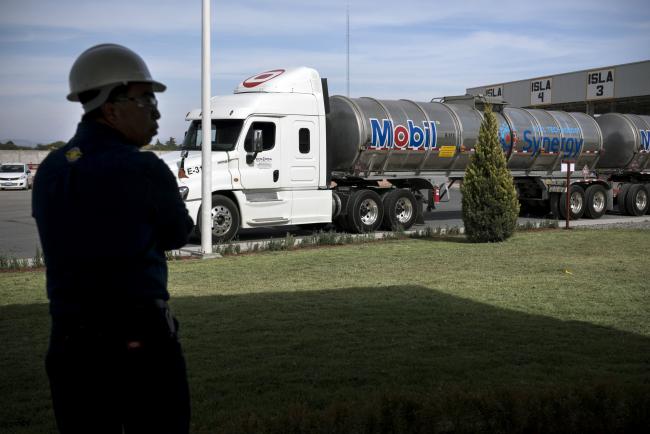 © Bloomberg. An employee stands in front of a fuel tanker during the unveiling of the Exxon Mobil Corp. fuel terminal in San Jose Iturbide, Mexico, on Wednesday, Dec. 6, 2017. Exxon Mobil Corp. is joining Chevron Corp. and other U.S. refiners to supply the newly free Mexican fuel market. Exxon Mobil indicated Wednesday that it will open 50 service stations by the end of first quarter and invest more than $300 million in Mexico's energy sector.