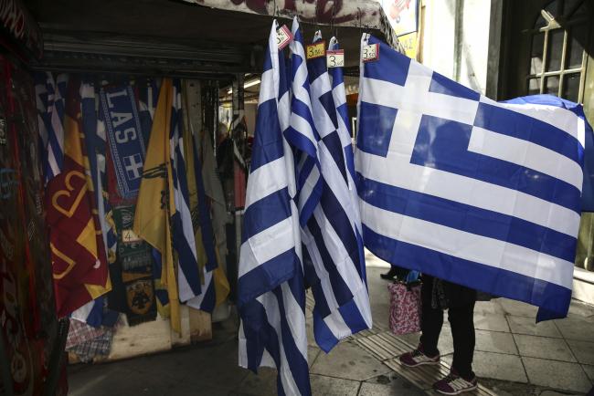 © Bloomberg. A woman unfolds a souvenir Greek national flag hanging outside a street vendor's kiosk in Athens, Greece, on Tuesday, Feb. 28, 2017. Greeces auditors are pulling together a list of policies the country needs to implement to unlock additional bailout funds as talks with Athens resumed on Tuesday, two people familiar with the matter said. 