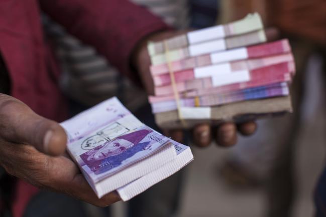 © Bloomberg. A roadside money changer handles bundles of Pakistani rupee banknotes at a currency exchange market in Karachi, Pakistan. 
