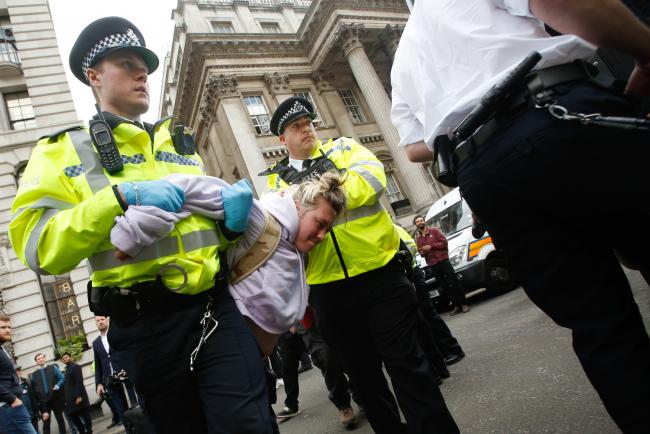 © Bloomberg. Police officers carry a climate activist during protests outside the Bank of England in the City of London on April 25. Photographer: Luke MacGregor/Bloomberg