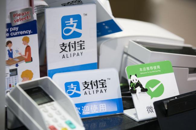 © Bloomberg. Signs for Ant Financial Services Group's Alipay, an affiliate of Alibaba Group Holding Ltd., center top and center bottom, and Tencent Holdings Ltd.'s WeChat Pay, right, are displayed at a Takeya Co. Ueno Select shop in Tokyo, Japan, on Saturday, Dec. 9, 2017. Ant Financial and its strategic partners outside China should be able to nearly double users of their payments systems in coming years, Ant's overseas operations president Douglas Feagin said on Nov. 14. 