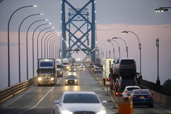 © Bloomberg. Commercial trucks and passenger vehicles drive across Ambassador Bridge on the Canada-U.S. border in Windsor, Ontario, Canada, on Thursday, Aug. 9, 2018. The Ambassador Bridge connects Canada to USA, from Windsor to Detroit and facilitates over 30% of all Canada-US road trade. 