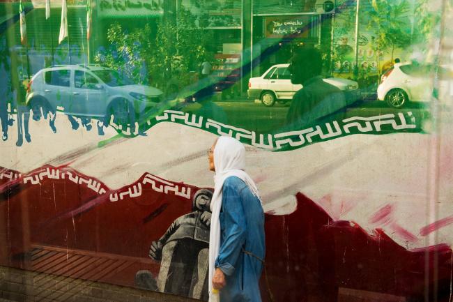 © Bloomberg. An elderly woman walks past a political wall mural outside the former U.S. embassy in Tehran, Iran, on Sunday, Aug. 5, 2018. Iran’s central bank, acting on the eve of U.S. sanctions, scrapped most currency controls introduced this year in a bid to halt a plunge in the rial that has stirred protests against the government of President Hassan Rouhani. Photographer: Ali Mohammadi/Bloomberg