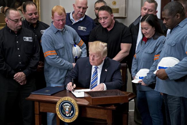 © Bloomberg. U.S. President Donald Trump signs a proclamation on adjusting imports of steel into the United States next to steel and aluminum workers in the Roosevelt Room of the White House in Washington, D.C., U.S., on Thursday, March 8, 2018.