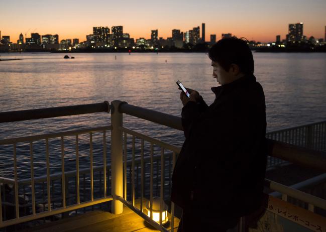 © Bloomberg. A man uses a smartphone at a pier in Tokyo, Japan, on Monday, Nov. 6, 2017. The Japanese Cabinet Office is scheduled to release third-quarter gross domestic product (GDP) data on Nov. 15, 2017.