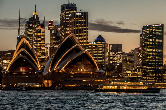 © Bloomberg. The Sydney Opera House, foreground, and buildings in the financial district stand illuminated at dusk in Sydney, Australia, on Friday, Sept. 29, 2017. A bungled transition from coal to clean energy has left resource-rich Australia with an unwanted crown: the highest power prices in the world. Photographer: Cole Bennetts/Bloomberg