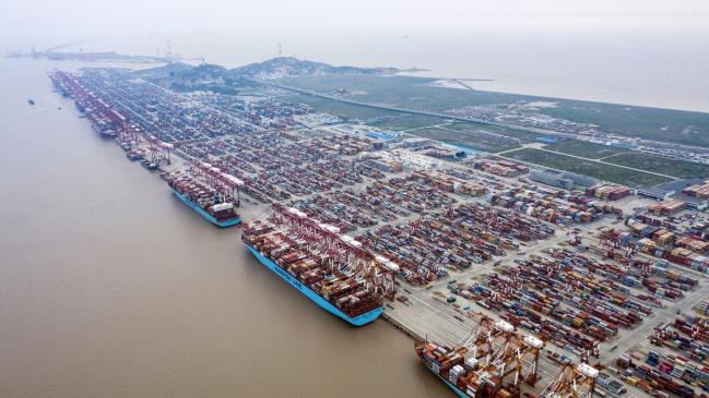 © Bloomberg. Container ships are docked next to gantry cranes as shipping containers sit stacked at the Yangshan Deepwater Port, operated by Shanghai International Port Group Co. (SIPG), in this aerial photograph taken in Shanghai. 