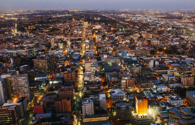 © Bloomberg. Commercial buildings and office property stand on the city skyline as night falls, as seen from the 50th floor of the Carlton Centre, in Johannesburg. 