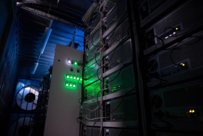 © Bloomberg. Green light illuminates the cases of mining rigs operating inside a shipping container converted into a mobile cryptocurrency mining farm, operated by BitCluster, at Rodniki Industrial Park in Rodniki, Russia, on Tuesday, Feb. 6, 2018. Cryptocurrencies have been pummeled by a wave of bad news, including the threat of more regulation from governments including the U.S., China, South Korea and India.