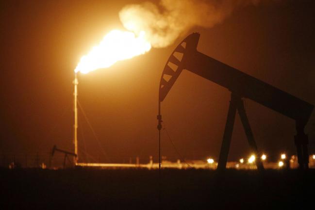 © Bloomberg. The silhouette of an electric oil pump jack is seen near a flare at night in the oil fields surrounding Midland, Texas, U.S., on Tuesday, Nov. 7, 2017. Nationwide gross oil refinery inputs will rise above 17 million barrels a day before the year ends, according to Energy Aspects, even amid a busy maintenance season and interruptions at plants in the U.S. Gulf of Mexico that were clobbered by Hurricane Harvey in the third quarter.