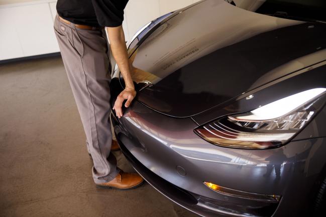 © Bloomberg. An employee closes the front hood of a Tesla Inc. Model 3 electric vehicle at the company's showroom in Newport Beach, California, U.S., on Friday, July 6, 2018. Tesla Inc. reached a milestone critical to Elon Musk's goal to bring electric cars to the masses -- and earn some profit in the process -- by finally exceeding a long-sought production target with the Model 3. Photographer: Patrick T. Fallon/Bloomberg