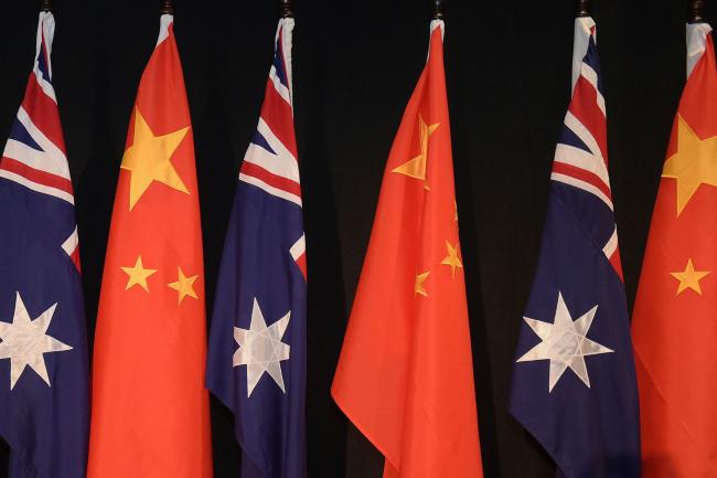 © Bloomberg. CANBERRA, AUSTRALIA - JUNE 17: A woman holding a copy of the Free Trade Agreement stands next to National flags of China and Australia during a signing ceremony on June 17, 2015 in Canberra, Australia. Hucheng is in Australia to formalise the free trade agreement between Australia and China. (Photo by Lukas Coch - Pool/Getty Images)