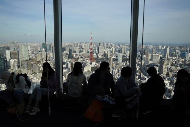 © Bloomberg. Visitors look out from the observation deck of the Roppongi Hills Mori Tower, operated by Mori Building Co., in Tokyo, Japan, on Monday, March 18, 2019. Amid intense debate on Japan’s inflation target, some officials at the central bank think the 2 percent goal will probably remain out of reach for the next three years, according to people familiar with the matter. Photographer: Toru Hanai/Bloomberg