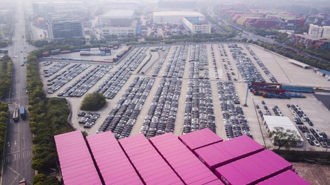 © Bloomberg. Vehicles stand at a port in this aerial photograph taken above Shanghai, China, on Monday, April 30, 2018. China won't succumb to 