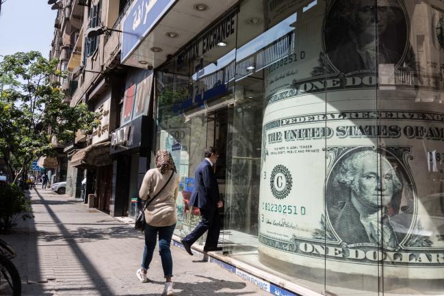 © Bloomberg. A pedestrian enters a currency exchange bureau adorned with a U.S. one dollar bill in Cairo, Egypt on March 31, 2018. Egyptian President Abdel-Fattah El-Sisi was set to sweep to victory with more than 90 percent of the vote in this week's election, crushing his one token challenger after credible competitors were eliminated before the contest. Photographer: Sima Diab/Bloomberg