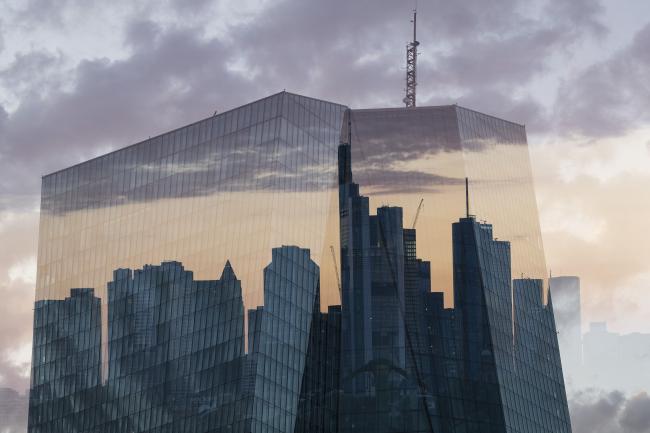 © Bloomberg. EDITORS NOTE: Multiple exposures were combined in camera to produce this image. An image of the European Central Bank (ECB) headquarters overlays the skyscraper skyline of the financial district in Frankfurt, Germany, on Monday, July 1, 2019. Following the collapse of merger talks between Deutsche Bank and Commerzbank, German Finance Minister Olaf Scholz changed his message from supporting a national champion to backing a cross-border merger. Photographer: Alex Kraus/Bloomberg