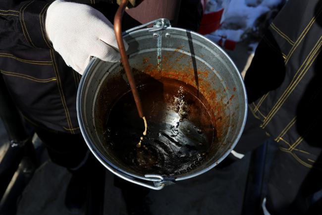 © Bloomberg. Workers use a bucket to collect a sample of crude oil at a multiple well platform, operated by Rosneft PJSC, in the Samotlor oilfield near Nizhnevartovsk, Russia.