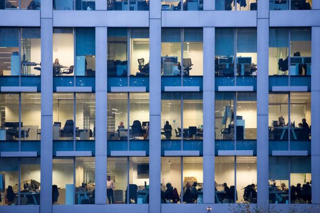 © Bloomberg. Office workers sit inside an illuminated office building in London, U.K., on Thursday, Nov. 22, 2018. Brexit Britain will be the top destination for major European investors to snap up commercial property next year, according to a survey of executives managing more than 500 billion pounds ($640 billion) of real estate conducted by Knight Frank. 