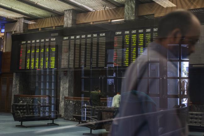 © Bloomberg. Traders and electronic stock boards are seen through a glass window at the Pakistan Stock Exchange (PSE) in Karachi, Pakistan, on Thursday, Feb. 8, 2018. The sell-off in global stocks that briefly looked to have ended mid-week has come back, tipping markets from the U.S. to Asia into declines exceeding 10 percent from their January highs.