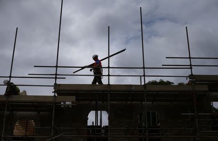 © Reuters. A builder assembles scaffolding as he works on new homes being built for private sale on a council housing estate, in south London