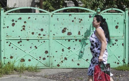 © Reuters. A woman walks past a gate filled with shrapnel holes, in Slaviansk