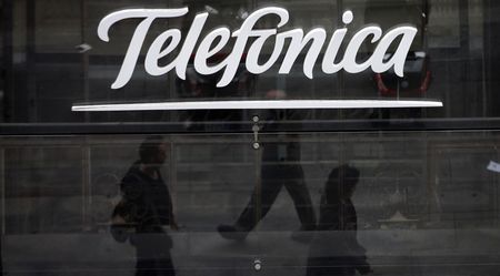 © Reuters. Passanti riflessi in una vetrina con il logo di Telefonica, nel centro di Madrid