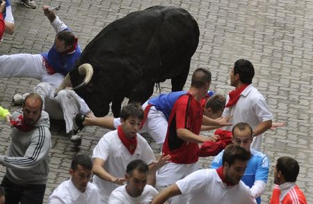 © Reuters. A runner gored in the leg by a Victoriano del Río fighting bull, falls at the entrance to the bullring during the third running of the bulls of the San Fermin festival in Pamplona