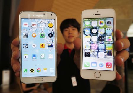 © Reuters. A sales assistant holding Samsung Electronics' Galaxy 5 smartphone and Apple Inc's iPhone 5 smartphone poses for photographs at a store in Seoul