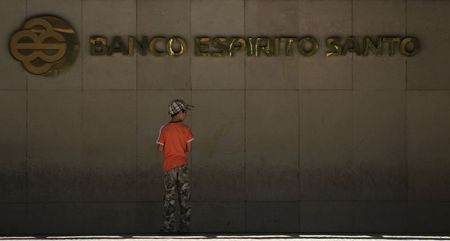 © Reuters. A boy stands in front of the logo of Portuguese bank BES at the bank's headquarters in Lisbon