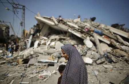 © Reuters. A Palestinian woman walks past the rubble of a residential building, which police said was destroyed in an Israeli air strike, in Gaza City