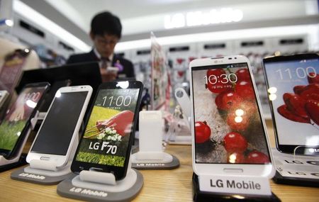 © Reuters. A sales assistant uses his mobile phone in front of mock LG electronics smart phones displayed at a store in Seoul