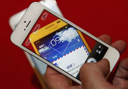 © Reuters. File photo illustration shows a man using an iPhone 5 to take a picture of a Samsung Galaxy Note smartphone in Beijing