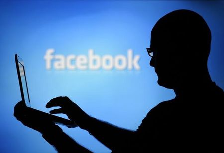 © Reuters. A man is silhouetted against a video screen with an Facebook logo as he poses with an Dell laptop in this photo illustration taken in the central Bosnian town of Zenica