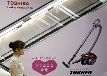 © Reuters. A woman rides an escalator past an advertisement for Toshiba Corp's vacuum cleaner in Tokyo