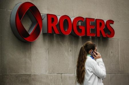 © Reuters. A woman speaks on her phone in front of a Rogers Communications Inc sign before the company's AGM in Toronto