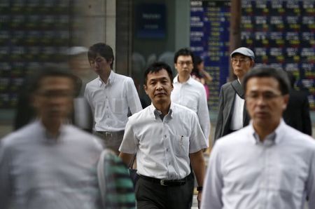 © Reuters. Tokyo, passanti davanti a un tabellone elettronico con l'andamento dei titoli azionari