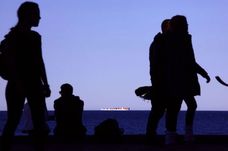 © Reuters. A container ship is seen on the horizon as pedestrians walk along a footpath past a couple sitting on a sea wall at Sydney's Manly Beach