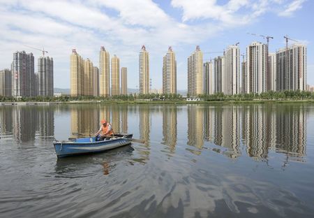 © Reuters. A man rows a boat on a river in front of new properties in Taiyuan