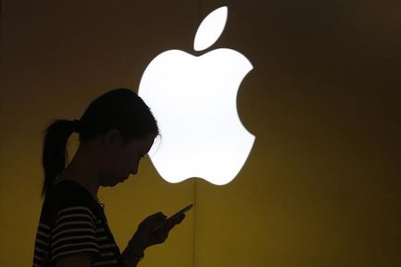 © Reuters. A woman looks at the screen of her mobile phone in front of an Apple logo outside an Apple store in downtown Shanghai