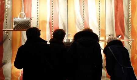 © Reuters. Shoppers look at luxury goods through a display window in downtown Milan