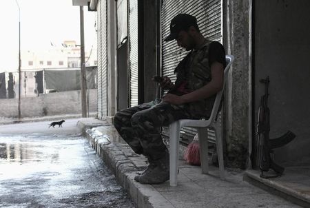 © Reuters. A Free Syrian Army fighter sits on a chair as he uses his mobile phone in Ashrafieh, Aleppo