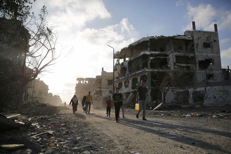 © Reuters. Palestinos caminham em meio a casas destruídas 