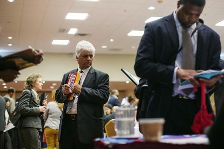 © Reuters. A man walks past job seekers as they fill out job applications for recruiters during a job fair in New York