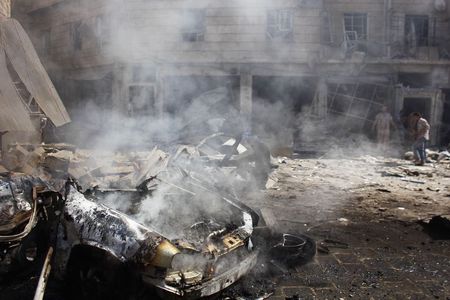 © Reuters. The wreckage of a burnt car is seen as people inspect a site hit by what activists said was a barrel bomb dropped at Qadi Askar district of Aleppo